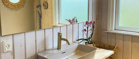 Un baño tipo cabaña de madera con lavamanos, espejo y ventana.