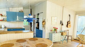 A kitchen with wooden cabinets, a dining table with placemats, a guitar, and a wicker chair. - Summer house near beach in Odder (Odder)