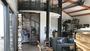 Ein modernes Interieur mit einer Wendeltreppe, einer Couch, Korbstühlen und einem Holzregal.