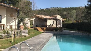 Ein Pool mit Holzterrasse, Steinhaus und Blick auf einen Hügel.