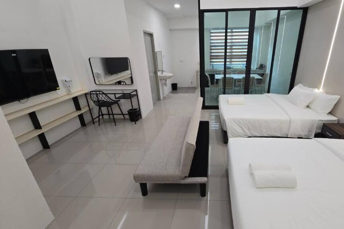 A modern hotel room with a TV, desk, two beds, and a glass door leading to a balcony.