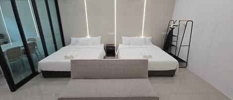 Una habitación de hotel moderna con dos camas, un banco, una partición de vidrio y un estante metálico.