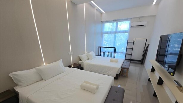 Una habitación de hotel moderna con dos camas, un banco, un televisor y un balcón con barandilla.