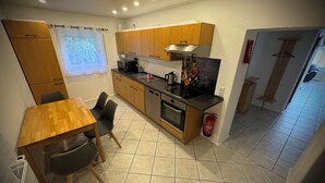 Eine kleine Küche mit Holzschränken, einer schwarzen Arbeitsplatte, einem eingebauten Ofen und einem Essbereich mit Holztisch und Stühlen.