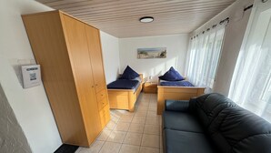 Ein Zimmer mit einem Bett, einer Schlafcouch, einem Holzschrank, einem kleinen Tisch und einem an der Wand befestigten QR-Code.