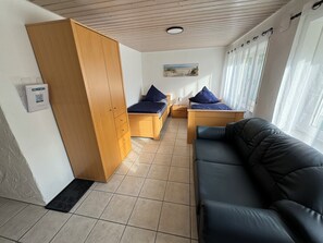 Ein Zimmer mit einem Bett, einer Schlafcouch, einem Holzschrank, einem kleinen Tisch und einem an der Wand befestigten QR-Code.