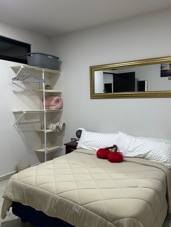 Un dormitorio con una cama, un espejo, una estantería y una cesta fijada a la pared.