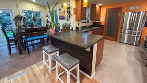 A modern kitchen with a central island, wooden bar stools, hanging plants, and stainless steel appliances. - Perfect Basecamp to explore the PNW and FIFA World Cup, easy walk to lightrail (Shoreline)