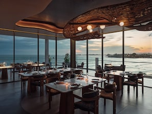 A restaurant with a view of the ocean, large windows, and a unique ceiling design.