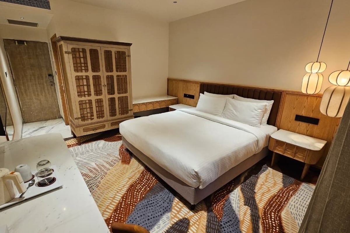 Une chambre d’hôtel comprenant un lit, des tables de chevet, une armoire, une salle de bain avec un miroir et un téléviseur.