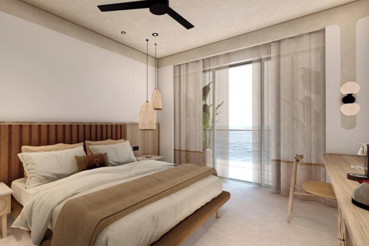 Une chambre à coucher moderne avec une tête de lit en bois, un lit recouvert d’une couverture beige, des tables de chevet, un bureau avec une chaise et un ventilateur de plafond.
