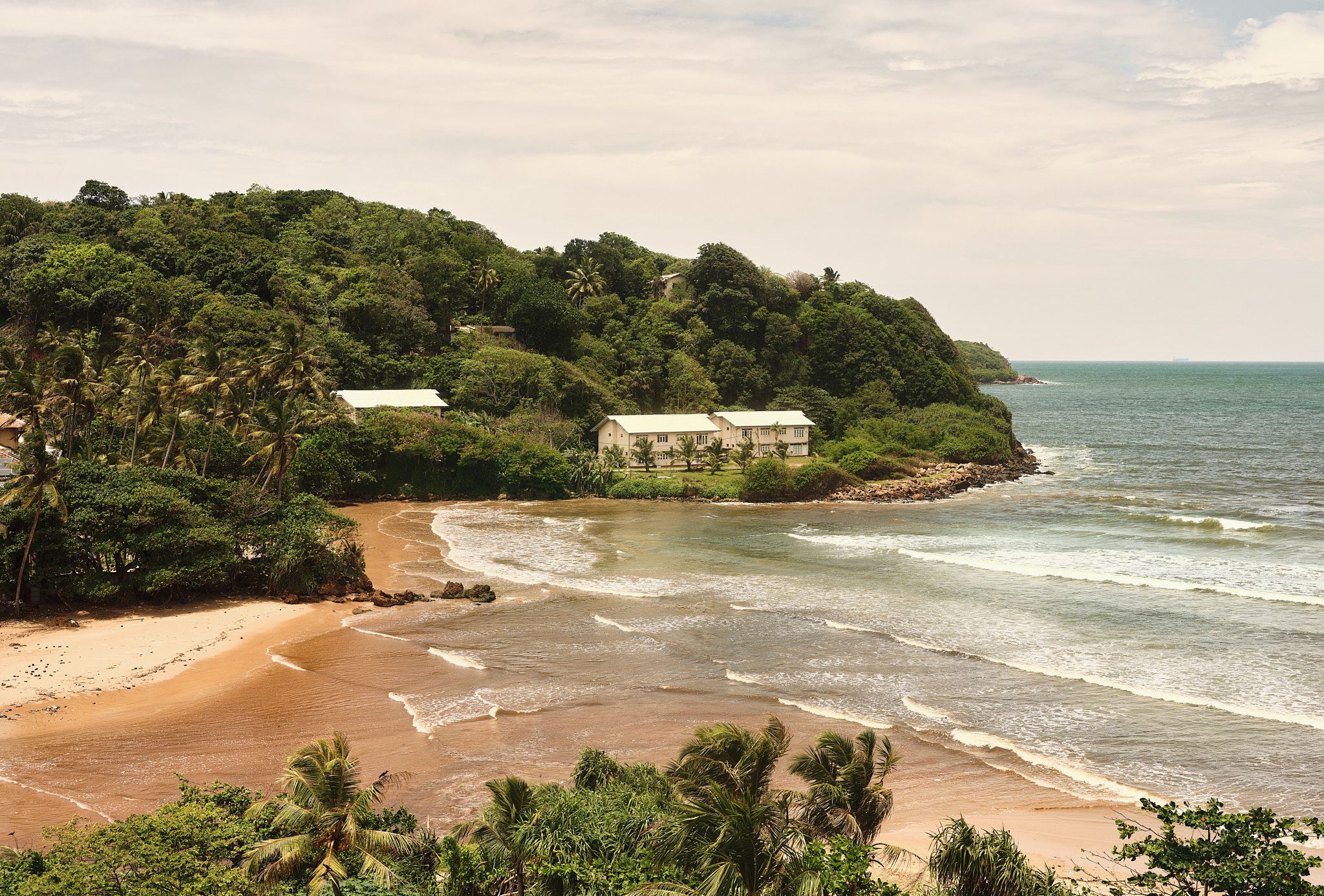A coastal property with a beach, a hill with buildings, and a view of the sea.