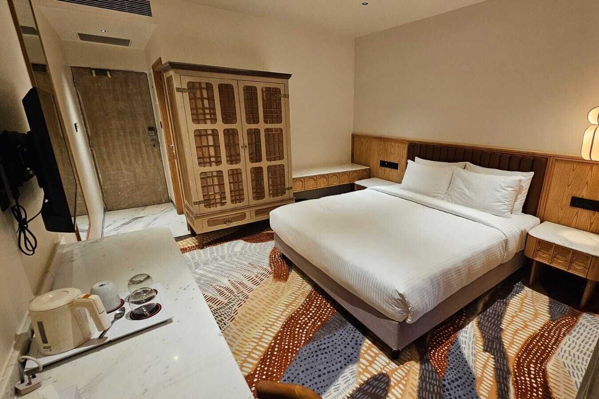 Une chambre d’hôtel comprenant un lit, une table de chevet, une commode, une armoire et une salle de bain avec un lavabo et un miroir.