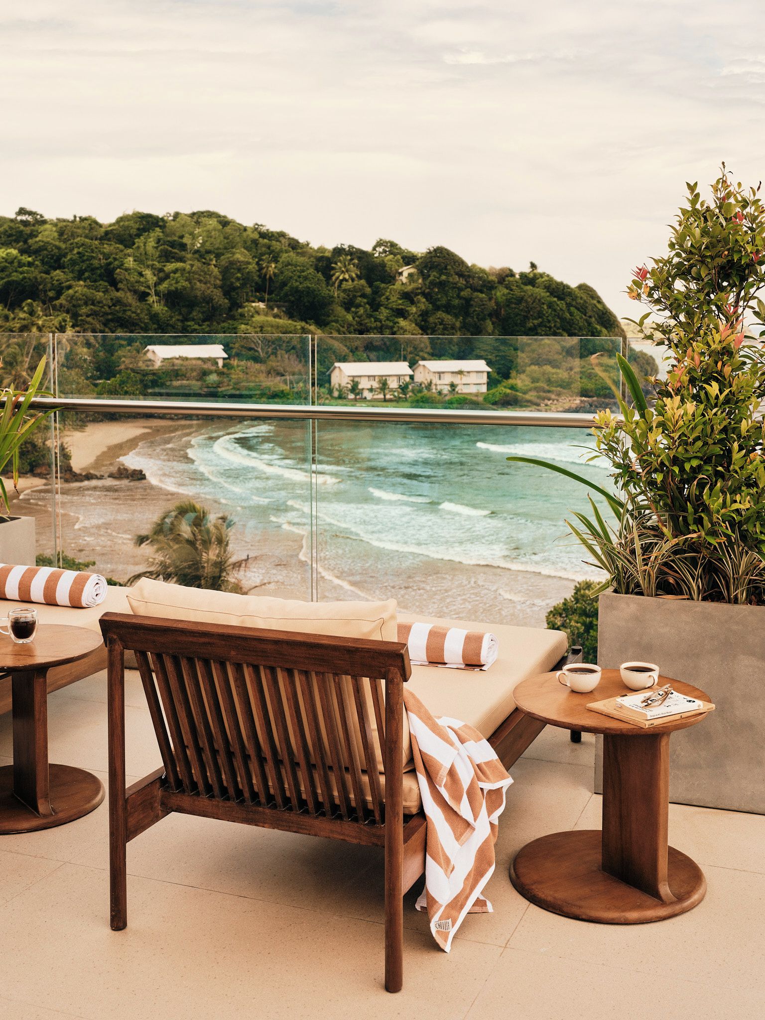 A terrace with a view of the ocean, a wooden chair, a table with a cup, and a plant.