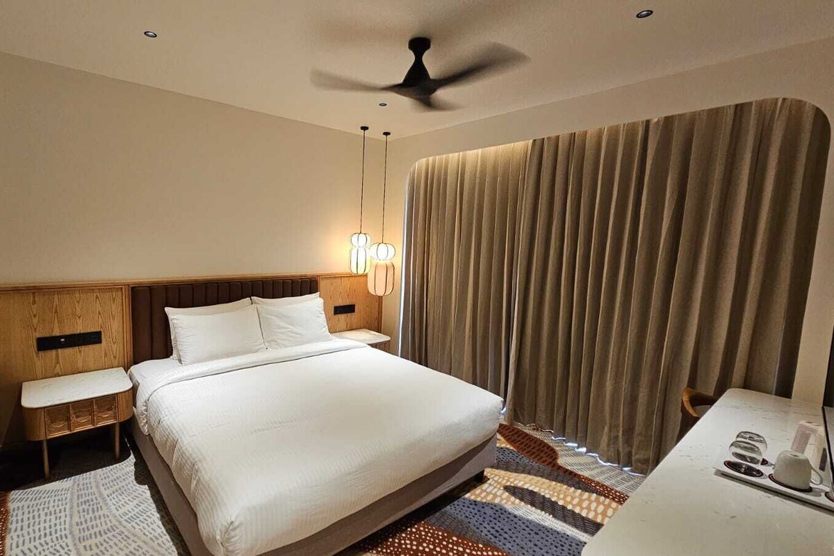 Une chambre d’hôtel comprenant un lit, des tables de chevet, un bureau, un ventilateur de plafond et des rideaux.