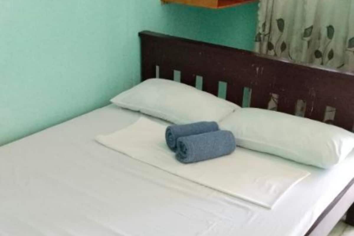 Un lit avec du linge de lit blanc et une serviette bleue, une tête de lit en bois et un mur de couleur turquoise.