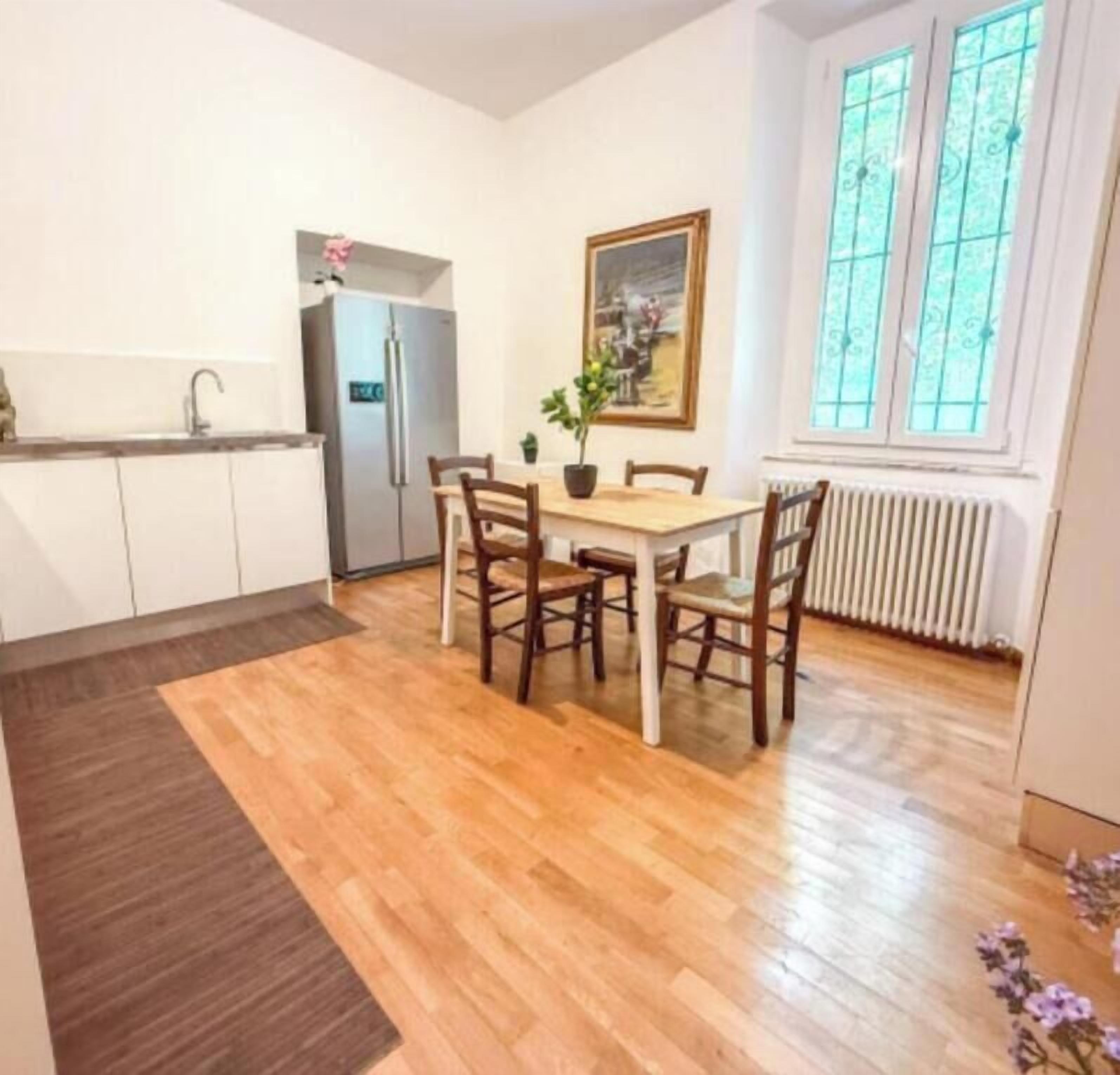 A compact kitchen with a refrigerator, a dining table with chairs, and a window with a view.