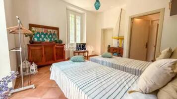 A bedroom with two beds, a wooden dresser, a desk, and a hanging light fixture.