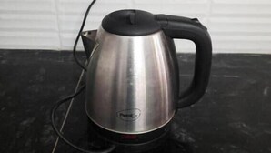 A stainless steel kettle with a black handle and cord on a black surface. - Saran Homestay (Agra)
