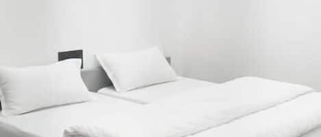 A modern, minimalist bedroom with a bed, pillows, and a nightstand.