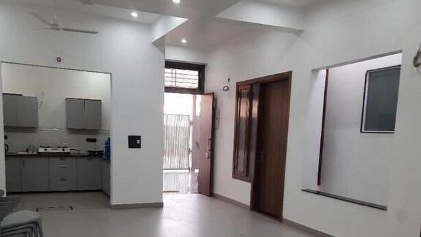 A spacious room with a kitchen area, a dining table with chairs, and a large window. - Saran Homestay (Agra)