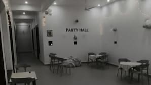 A spacious room with a high ceiling, recessed lighting, and a sign indicating it is the party hall. Tables and chairs are arranged for dining. - Saran Homestay (Agra)