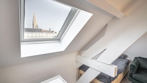 A room with a skylight, a loft bed, and a view of a building with a tower. - Cosy 1-bedroom Apartment, Antwerp (Antwerp)