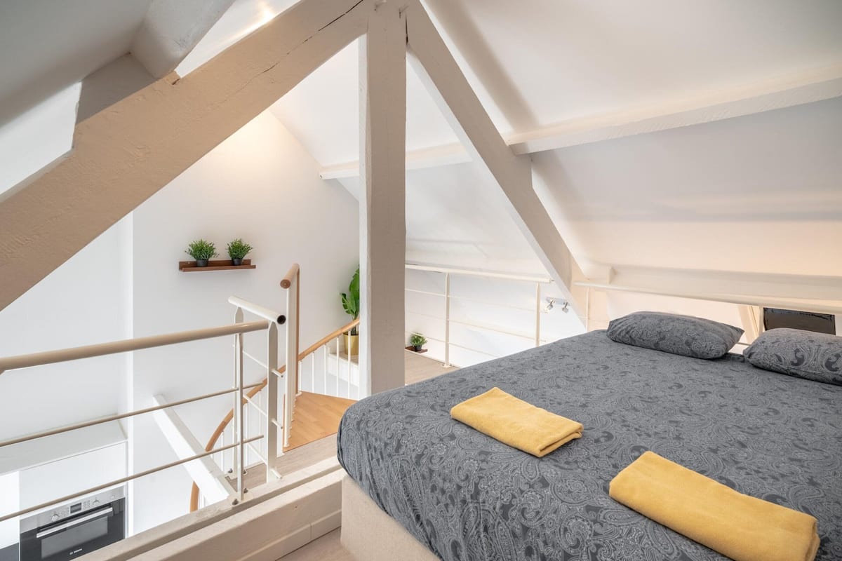 Quarto com cama, toalha amarela, escada e uma pequena planta na parede.