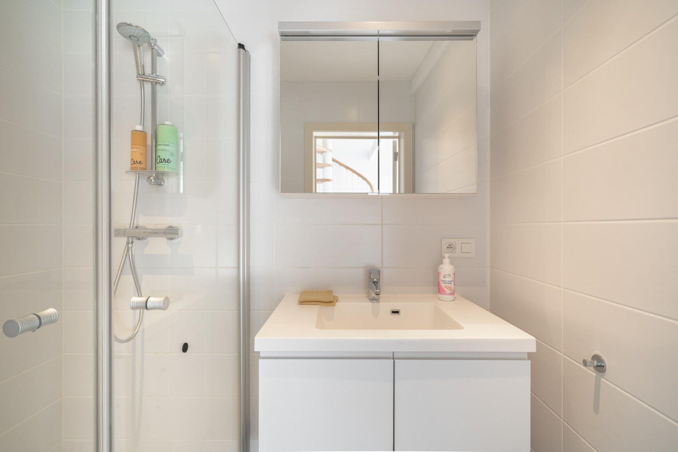 A bathroom with a glass shower enclosure, a white sink with a mirror above it, and toiletries on the sink.