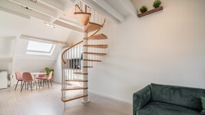 A modern interior with a spiral staircase, a dining area with pink chairs, and a green sofa. - Cosy 1-bedroom Apartment, Antwerp (Antwerp)
