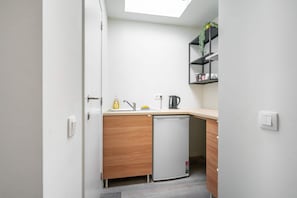 A compact kitchen with a dishwasher, a sink, a kettle, and a small shelf with a plant.