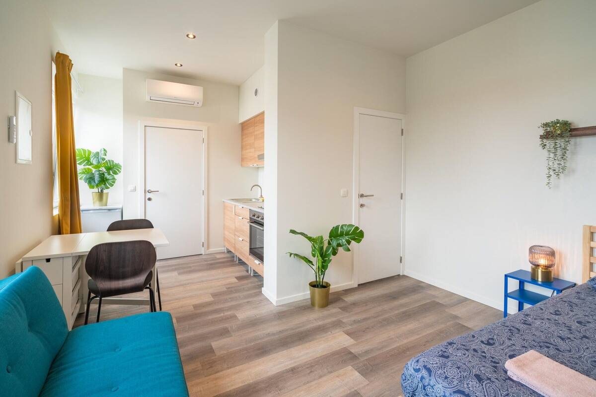 A modern apartment with a dining area, kitchenette, and a bedroom with a bed and bedside table.