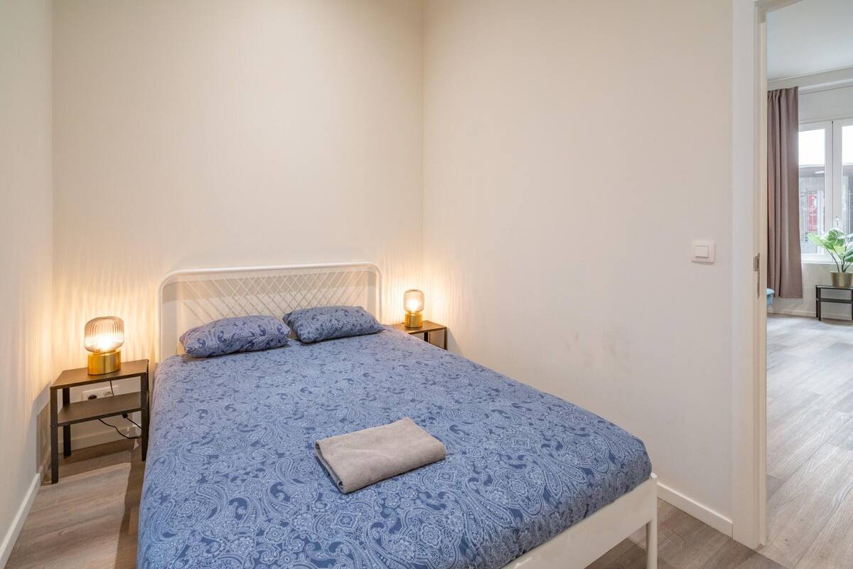 A bedroom with a bed, bedside lamps, and a view into another room.