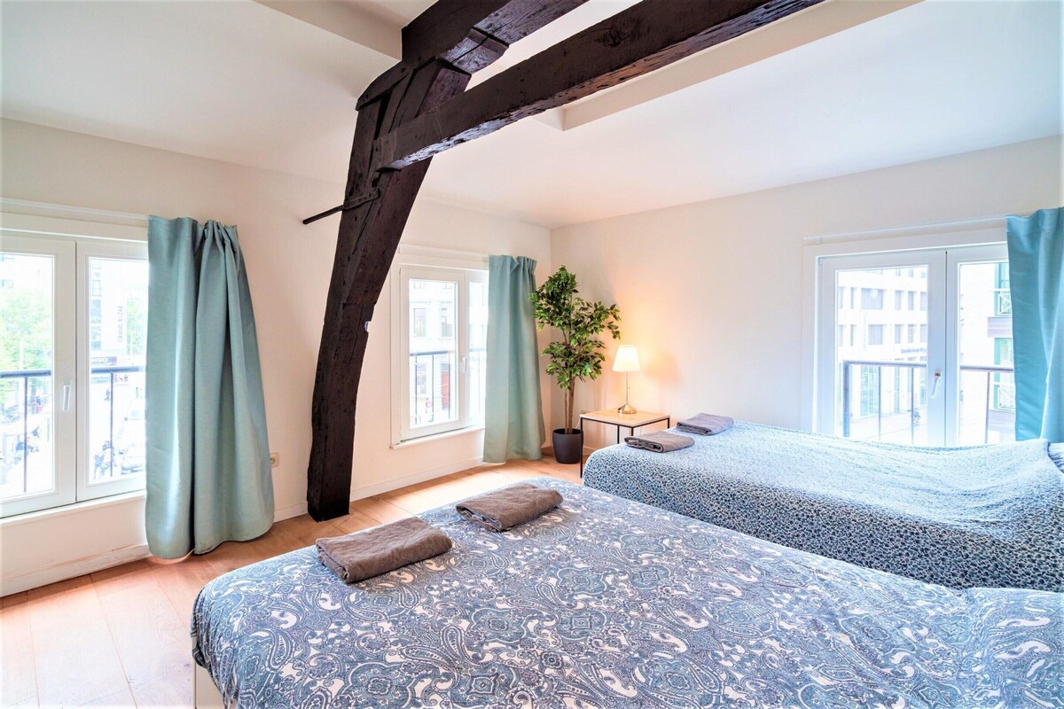 A bedroom with two beds, a window, a plant, and a lamp.