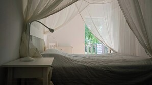 Un dormitorio con cama, mesita de noche con lámpara y cortinas traslúcidas.