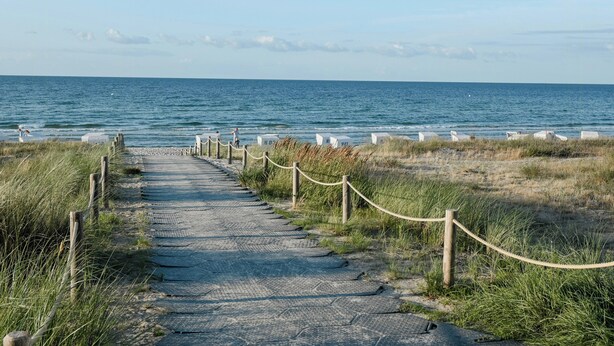 Un camino costero que lleva al mar, con una barandilla de cuerda y postes de madera.