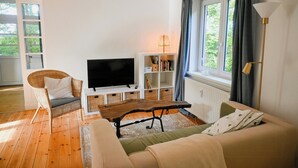 Una sala de estar con televisor, sillón de mimbre, sofá y estantería.