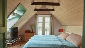 Une chambre avec un plafond en pente, un lit, une télévision, un bureau et une fenêtre.