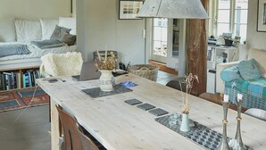 Un loft spacieux avec un plafond haut, des poutres apparentes, une longue table à manger avec des chaises, un canapé et un escalier menant à un niveau supérieur.
