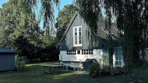 Une maison avec une grande fenêtre, un barbecue couvert et une table dans la cour.