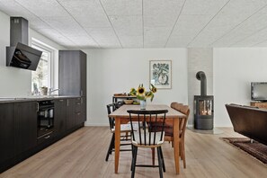 Una cocina moderna con armarios oscuros, una zona de comedor con mesa y sillas de madera, una estufa empotrada y un televisor de pantalla plana montado en la pared.