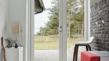 Een modern interieur met een witte muur, een rode bank, een wit bureau en uitzicht door een glazen deur op een buitenruimte.