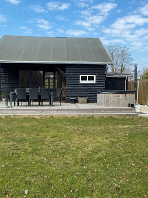 Een houten blokhut met een overdekt terras, buitenmeubilair en een omheinde tuin.