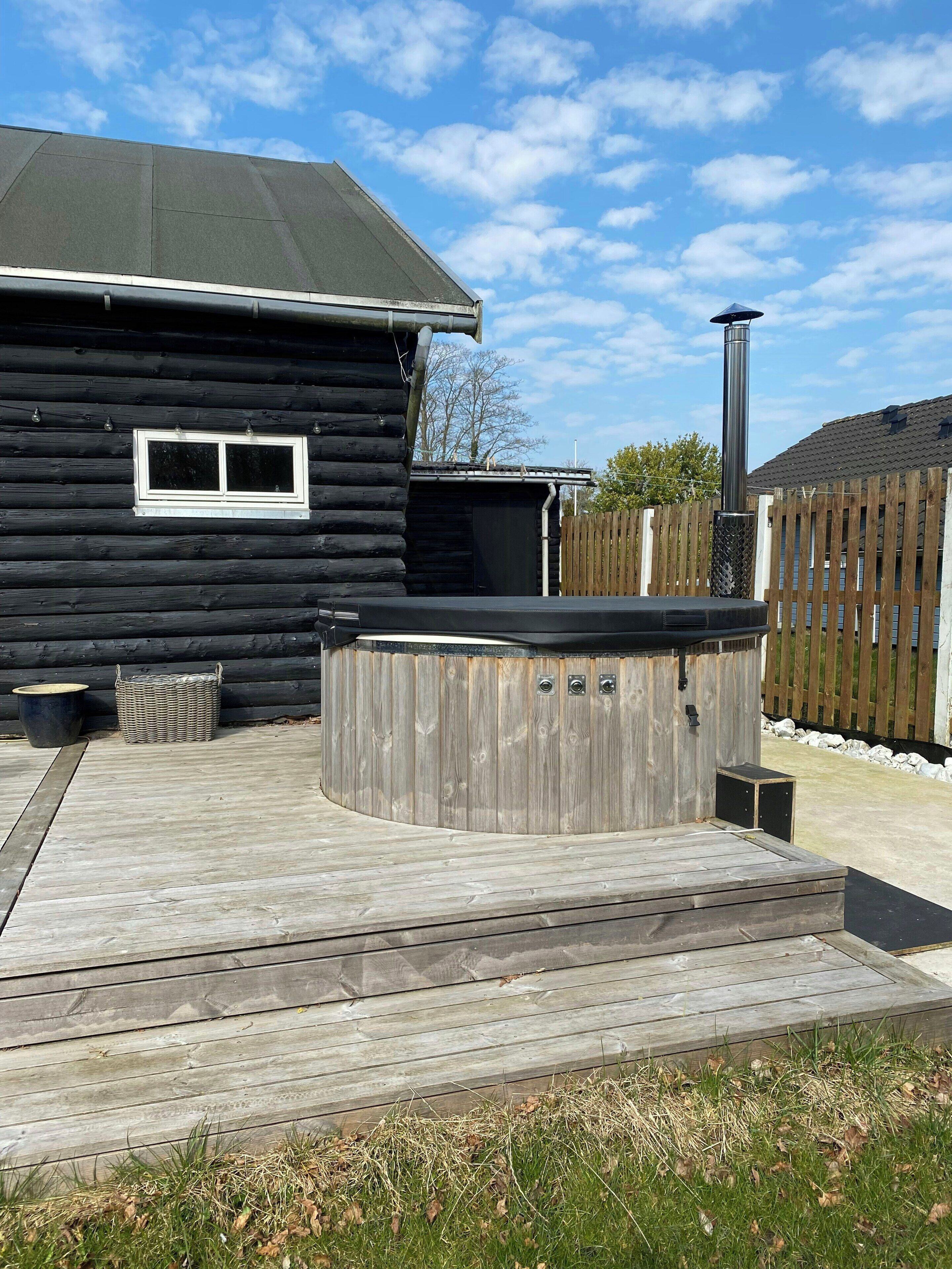 Een houten hut met een jacuzzi, een raam en een terras.