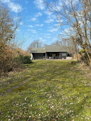 Een rustiek gebouw met een ruime open veranda, omgeven door bomen en een gazon.