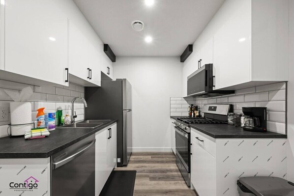 Una cocina moderna con armarios blancos, encimera negra, electrodomésticos de acero inoxidable y un logotipo visible en el salpicadero.