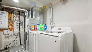 A laundry room with a washing machine, a dryer, and various cleaning supplies. - Orchards Delight | Near Airport | Sleeps 4 | WiFi (Edmonton)