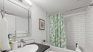 A bathroom with a white sink, a mirror, a shower curtain with a leaf pattern, and a small potted plant. - Orchards Delight | Near Airport | Sleeps 4 | WiFi (Edmonton)