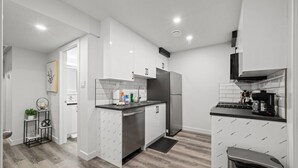 A modern kitchen with white cabinetry, a stainless steel refrigerator, and a black countertop. - Orchards Delight | Near Airport | Sleeps 4 | WiFi (Edmonton)