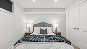 A bedroom with a bed, two bedside tables with lamps, a headboard, and a door. - Orchards Delight | Near Airport | Sleeps 4 | WiFi (Edmonton)